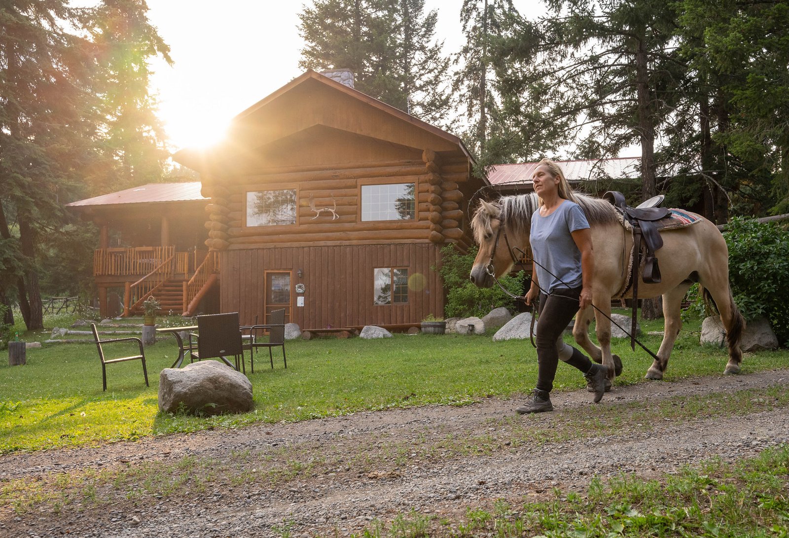 Eine Frau führt ein Pferd am Halfter vor einem Blockhaus